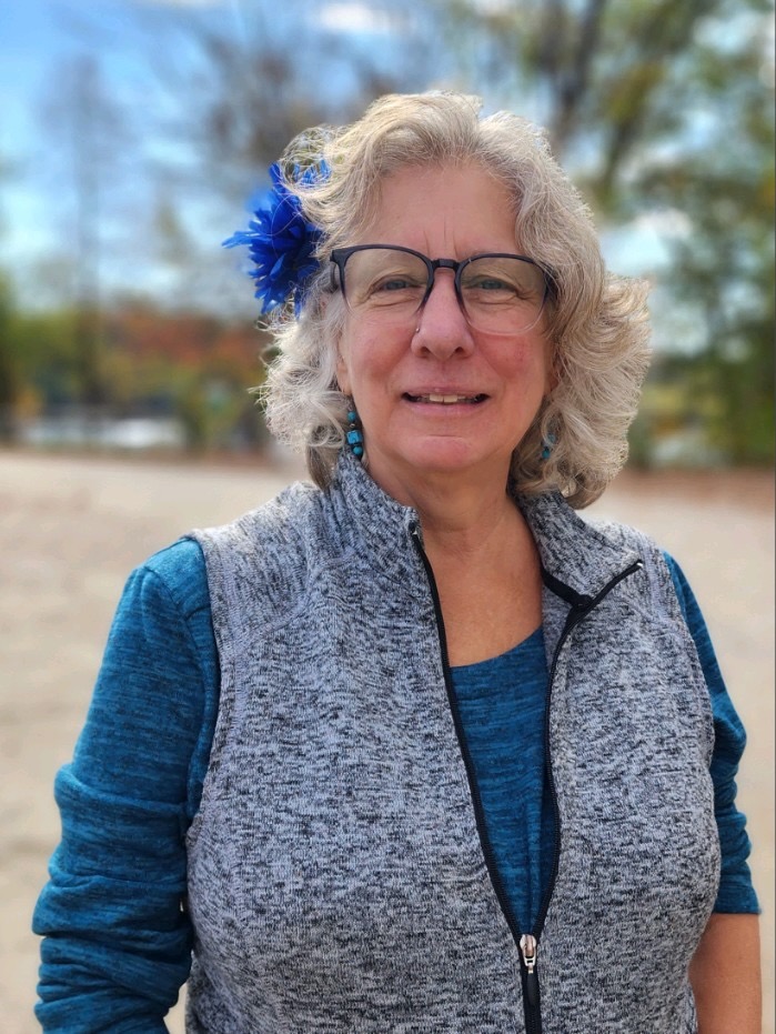 Full Color headshot of Director Julianna Dodson of Radically Rural.  She is standing next to a large industrial window in a nondescript commercial building, leaning on the sill and smiling directly into the camera.